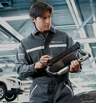 Skilled BMW Service technician with handheld computer and wearing gray BMW Service jumpsuit