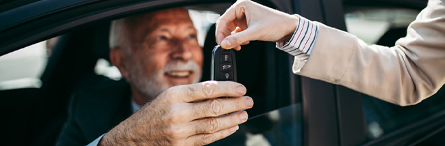 man sitting in car being handed car key, and he is smiling