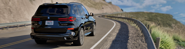 Back view of a black BMW SVu drinving on a road on a mountain side