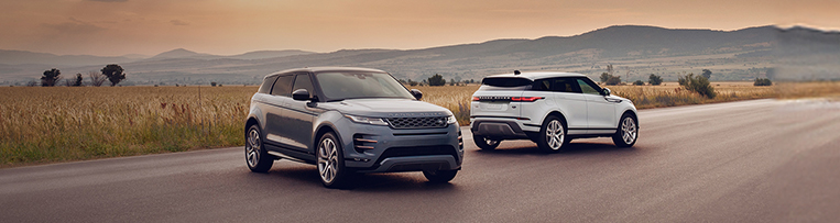 Two Land Rover parked on a road with mountains in the background